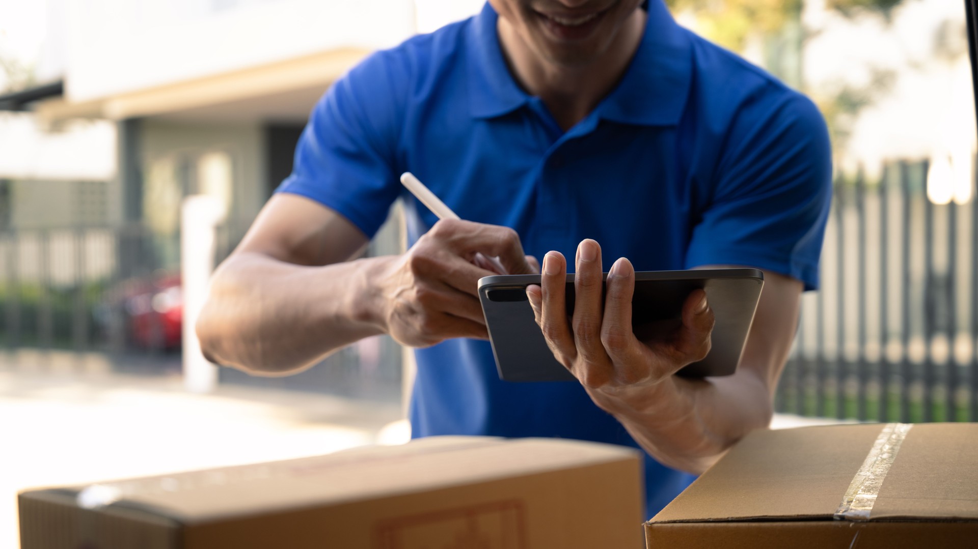 Cropped shot of delivery man in blue uniform using digital tablet while standing at open van full of delivering package.